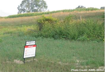 A "For Sale" sign next to farm land.